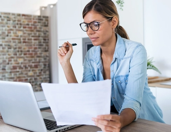 Chica comparando unos documentos mientras mira su ordenador portátil